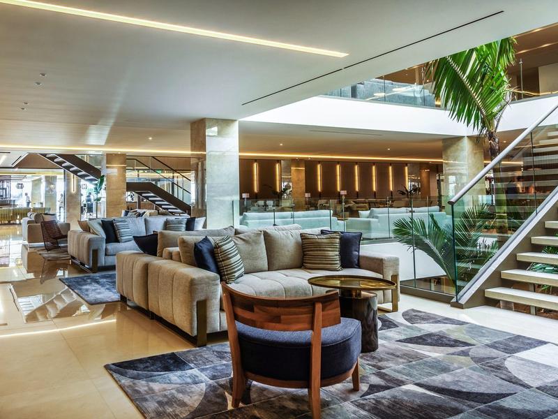 Großer moderner Wohnbereich mit Sofas, Sesseln, Teppich und Treppe mit Glasgeländer.