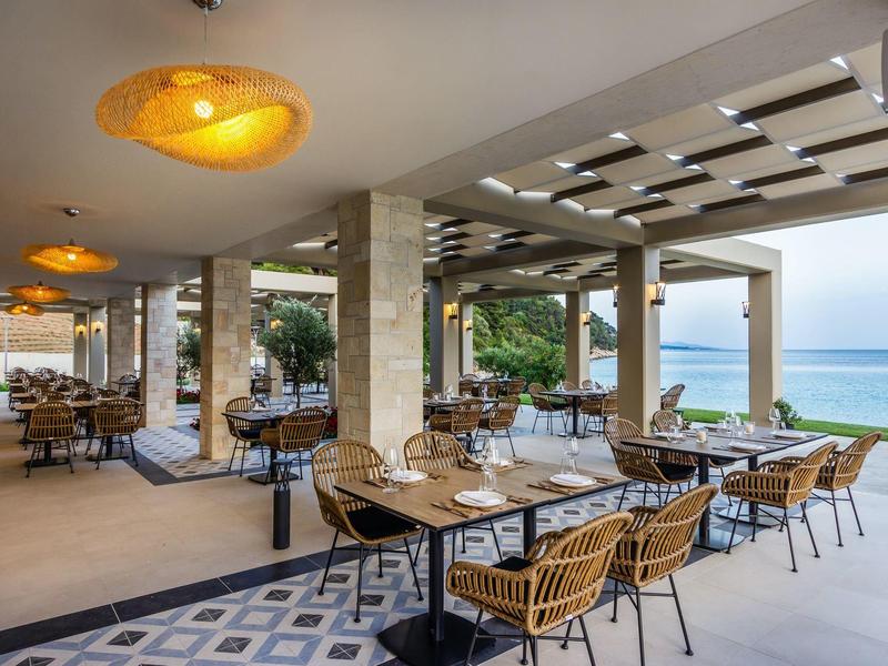 Offenes Restaurant mit Stühlen, Tischen, moderner Deckenbeleuchtung und Meerblick bei Tageslicht.