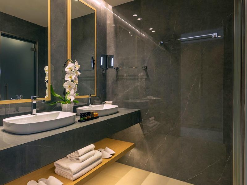 Modernes Badezimmer mit schwarzer Wand, Waschtisch, rundem Spiegel und beleuchtetem Ablagefach.