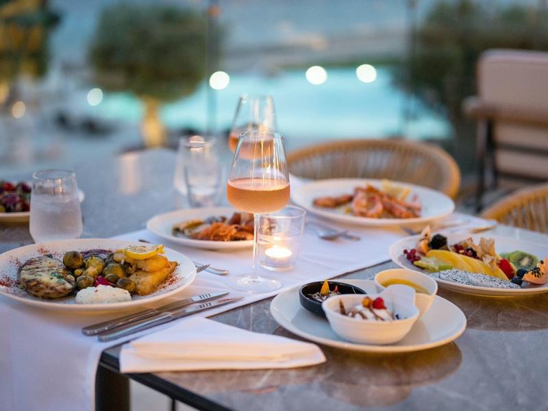 Ein gedeckter Tisch mit bunten Speisen, Gläsern und Kerzen in gemütlicher Atmosphäre am Abend.