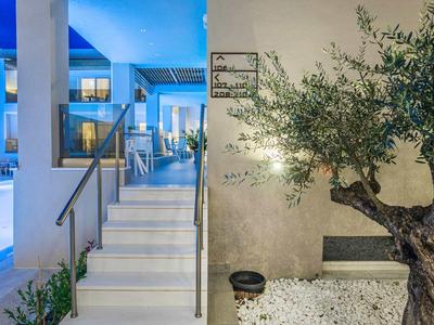 Modern hotel entrance with stairs, handrail, and illuminated tree in gravel bed at dusk.