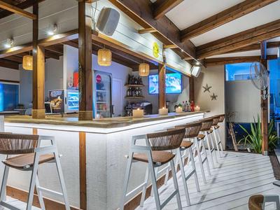 Modern hotel bar area with white stools and wooden ceiling beams in daylight.