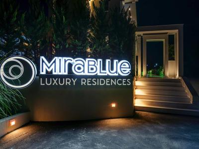 Illuminated Mirablue Luxury Residences sign beside an entrance with stairs at night