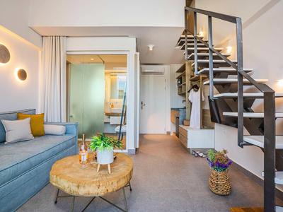 Chambre d'hôtel moderne avec escalier, canapé, cloison en verre et coin salon aux tons neutres.