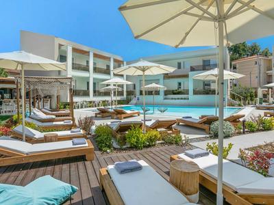 Modern hotel pool area with loungers, umbrellas, and well-maintained plants under a blue sky.