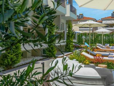 Sunny hotel terrace with white lounge chairs and wooden decor next to a building.