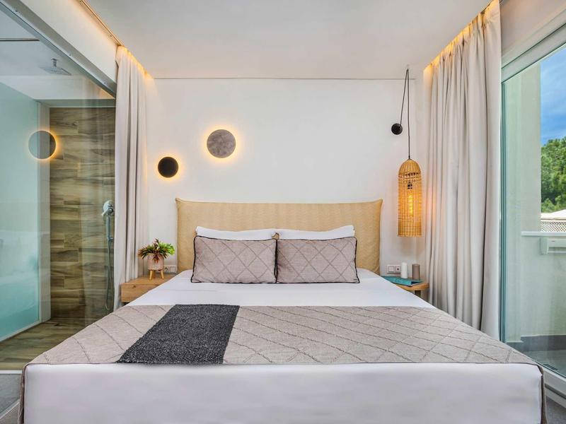 Chambre d'hôtel moderne avec lit double, éclairage doux et vue sur des collines vertes.