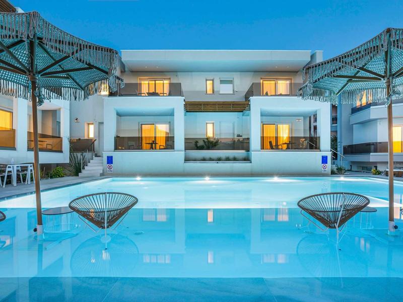 Piscine d'hôtel moderne avec chaises longues et parasols sous un ciel clair.