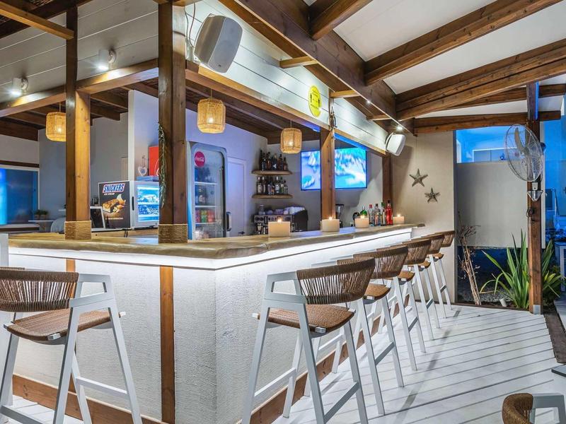 Bar extérieure moderne avec tabourets en bois et comptoir éclairé sous un toit en bois.