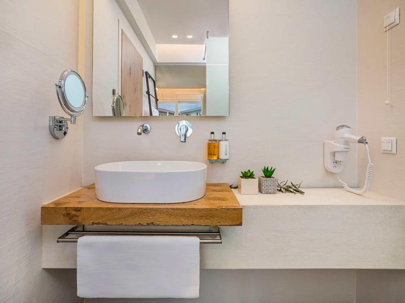 Salle de bain moderne avec lavabo, miroir et étagère en bois dans un design clair.