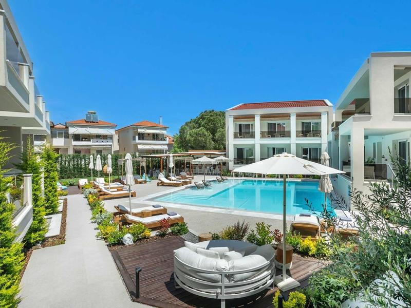Espace piscine d'hôtel moderne avec transats, parasols et bâtiments blancs environnants sous un ciel clair.