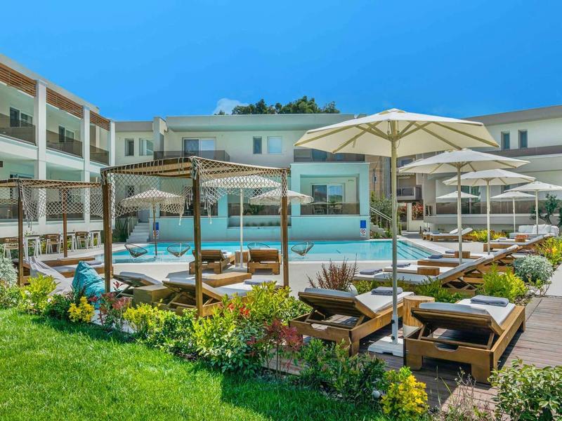 Zone de piscine d'hôtel avec chaises longues, parasols et pelouse verte sous un ciel clair