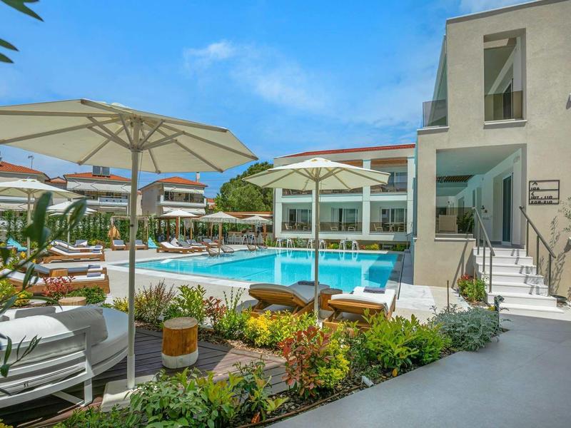 Espace piscine extérieur moderne d'un hôtel avec chaises longues et parasols sous un ciel clair.