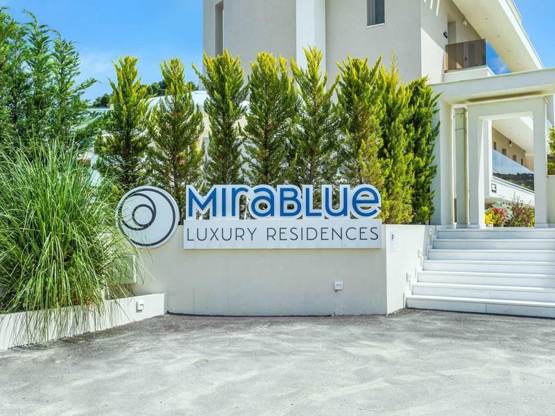 Entrée de Mirablue Luxury Residences avec escaliers et végétation dense.