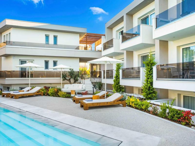 Espace piscine d'hôtel moderne avec chaises longues et parasols sous un ciel clair.