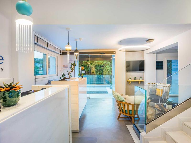 Intérieur d'hôtel lumineux et moderne avec comptoir, coin salon et vue sur un espace extérieur verdoyant.