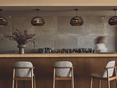 Moderner Hotelbarbereich mit drei Stühlen, hängenden Lampen und einer Vase auf der Theke.