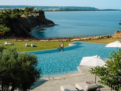 Infinity zwembad met ligstoelen met uitzicht op rustige baai en kliffen onder heldere lucht