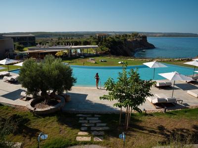Blick auf einen Swimmingpool mit Liegestühlen, Sonnenschirmen und Meer in der Ferne bei klarem Himmel