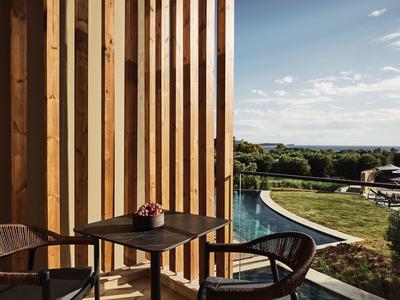 Balkon mit Holzverkleidung, Tisch, Stühlen und Blick auf Pool und Landschaft bei klarem Himmel.