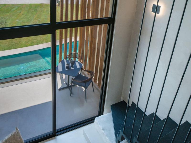 Moderne binnenruimte met trap en uitzicht op terras met zwembad en buitenstoelen.