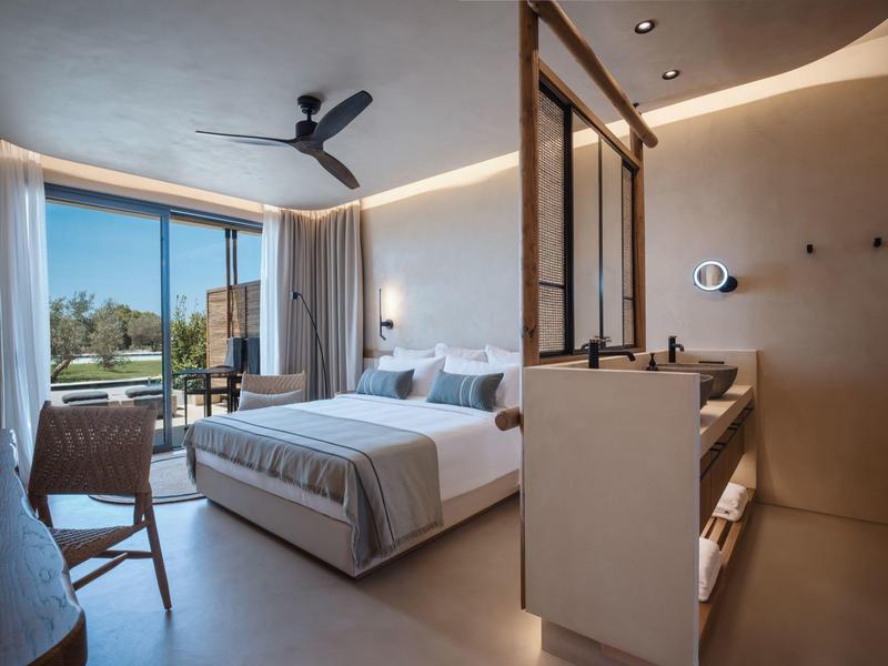 Moderne hotelkamer met groot bed, stoel en panorama raam met uitzicht op de natuur.