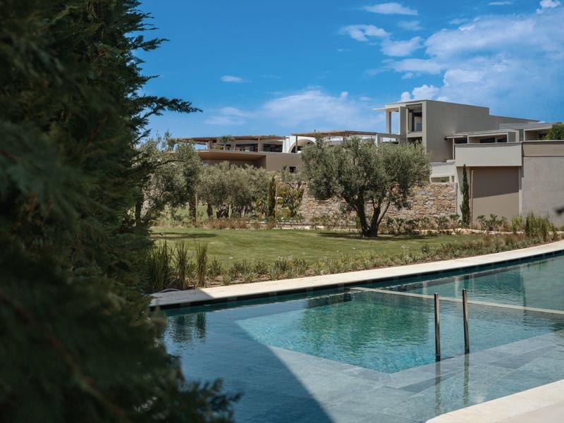 Modern hotelzwembad met bomen en moderne gebouwen onder een blauwe lucht.