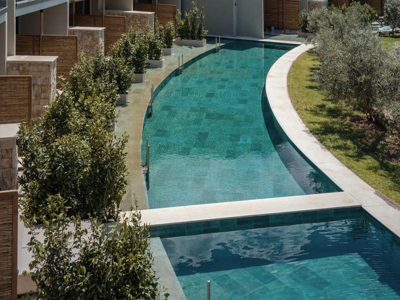 Moderne hotelzwembad met helder blauw water, omgeven door planten en gebouwen.