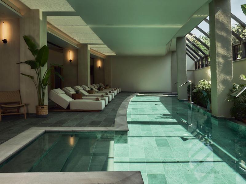 Moderne binnenzwembad met ligstoelen en glazen ramen die daglicht binnenlaten.