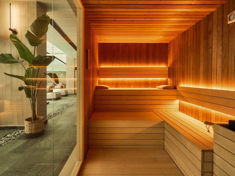 Moderne sauna met houten bekleding, indirecte verlichting en uitzicht op aangrenzende kamer met planten.