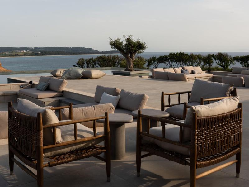 Gemütliche Outdoor-Lounge mit Korbsesseln und Sofas mit Meerblick bei Sonnenuntergang.