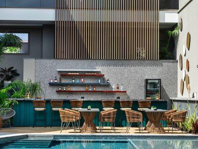 Moderner Außenbereich eines Pools mit Bar, Holzstühlen und grüner Bepflanzung bei Tageslicht.