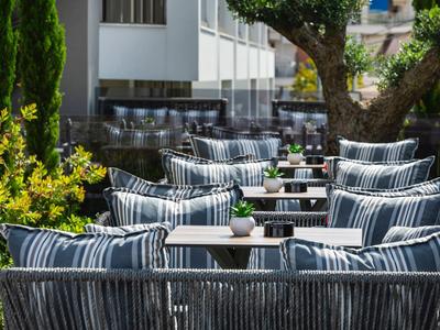 Strefa na zewnątrz hotelu z miejscami do siedzenia i pasiastymi poduszkami pod drzewami.