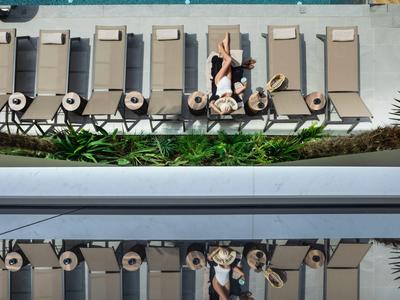 Blick von oben auf Liegestühle neben einem Pool mit zwei Personen auf einer Liege.
