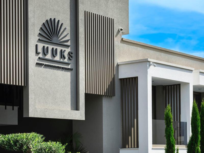 Elewacja nowoczesnego hotelu z napisem LUUKS i jasnym niebieskim niebem w tle.