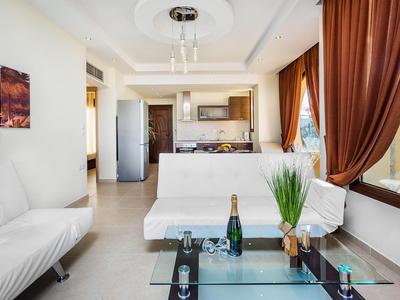 Modern living room with kitchenette, white furniture, and large brown curtains.