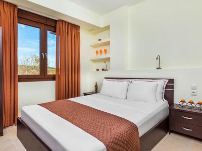 Bright hotel room with double bed, nightstand, and large window with brown curtains.