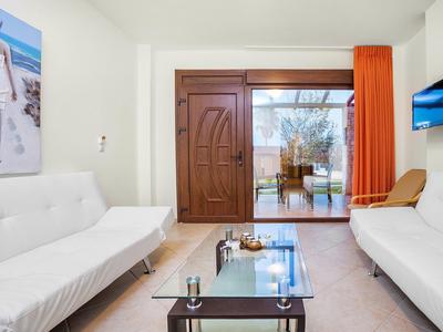 Bright living room with white sofas, glass table, and terrace access overlooking the sea.