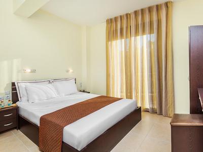 Bright hotel room with double bed, nightstands, and curtains at the window.