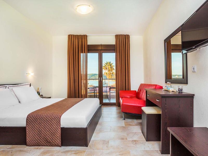 Modern hotel room with double bed, red sofa, and balcony overlooking palm trees.