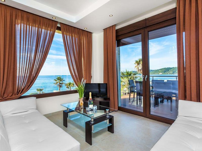 Modern hotel room with white sofas, glass coffee table, and balcony with sea view.