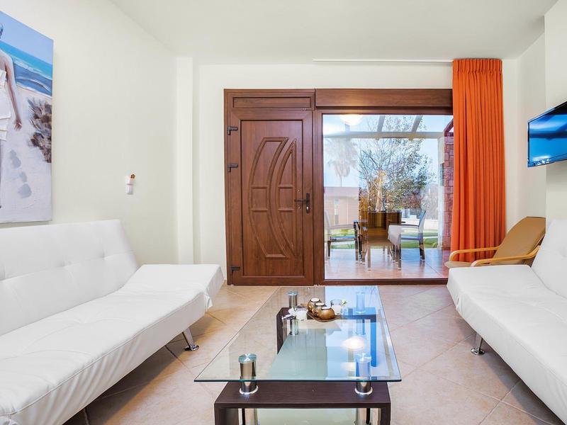 Bright living room with white sofas, glass table, and terrace access overlooking the sea.