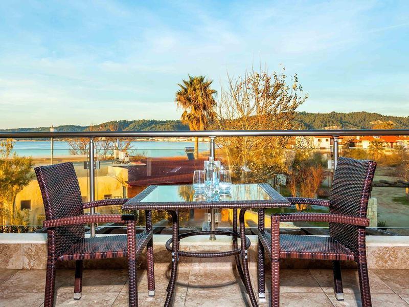 Two chairs and a table on a balcony with a view of a coastal landscape at sunrise.