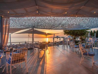 Eleganter Außenbereich eines Hotels mit gedeckten Tischen und Blick auf den Sonnenuntergang am Meer.