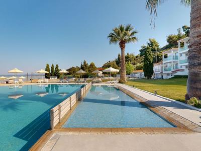 Moderne Poolanlage mit Flachwasserbereich, Palmen und weißen Sonnenschirmen neben Hotelgebäuden.