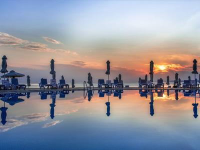Spiegelglatter Pool mit Sonnenschirmen und Sitzgelegenheiten im Sonnenuntergang.