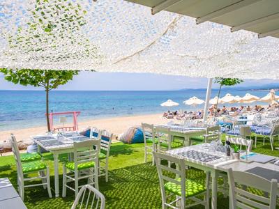Freier Strandblick mit weißen Stühlen und Tischen unter Sonnensegeln nahe blauem Meer und Sandstrand.