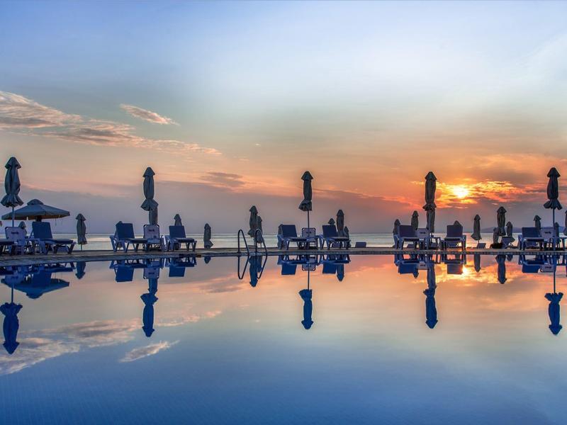 Ein ruhiger Pool spiegelt die bunten Wolken des Sonnenuntergangs und geschlossene Sonnenschirme wider.