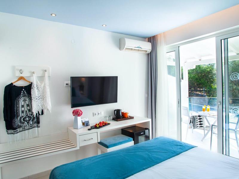 Helles Schlafzimmer mit TV, weißer Wand, blauem Bett und großer Glasschiebetür zum Balkon.