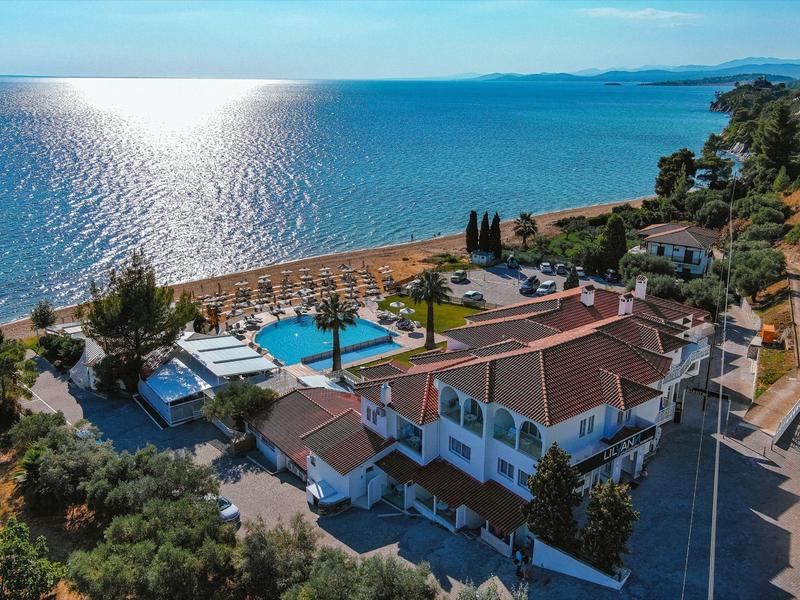 Villa mit Pool an Küste, umgeben von Bäumen, nahe blauem Meer unter klarem Himmel.
